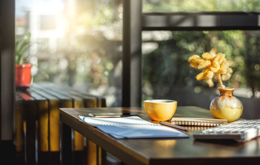 Place of work on wooden desk with cup of coffee, notebook, mobile phone and computer keyboard. Background vintage tone