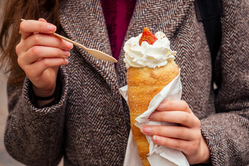 woman with an appetite eats a traditional Czech sweet Trdelnik with vanilla cream and strawberries ,useing eco wooden spoon in Prague street