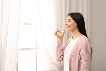 Wall Mural - Beautiful young woman drinking fresh lemon water indoors