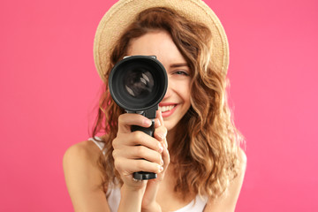 Wall Mural - Beautiful young woman using vintage video camera against crimson background, focus on lens