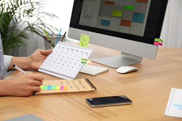 Woman making schedule using calendar at table in office, closeup