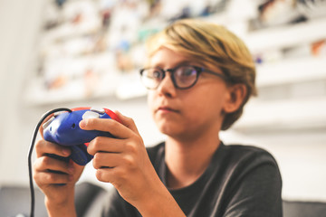 Boy sitting on sofa, playing with game console online with friends. Teen on the couch makes grimace while engaged with a video game. Addicted gamer enjoy the challenge. Addiction, dependence concept.