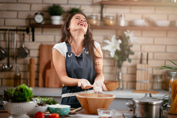 Wall Mural - Young woman in kitchen. Beautiful woman having fun while making  dough.