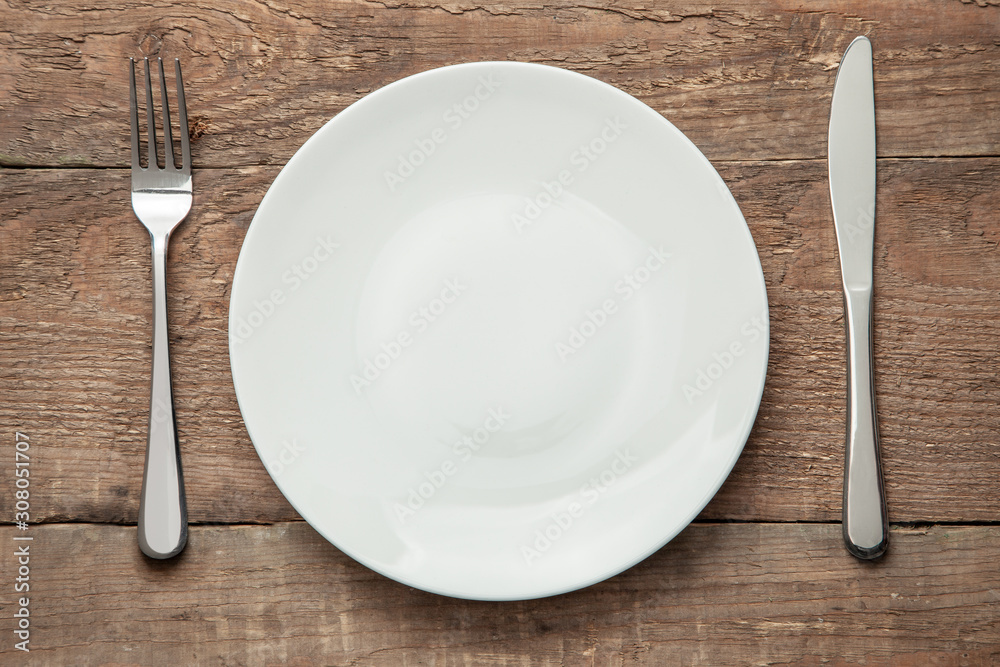 Empty white plate with knife and fork on a wooden table - obrazy, fototapety, plakaty 