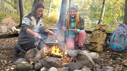 female friends cooking traditional pancakes over an open fire in the camp outdoor, enjoying the sile