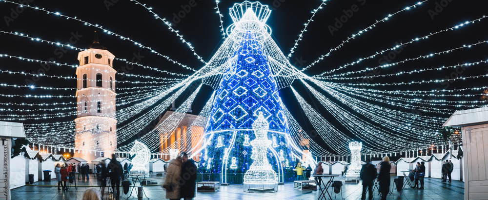 Obraz na płótnie Vilnius, Lithuania, 2019: Beautiful Christmas tree decorated with white and blue lights chess queen for Christmas 2019 and New Year 2020, market and celebrations in Vilnius Cathedral square, panorama. w salonie
