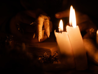 Divination with the help of chicken feet and dry herbs. The light from the candles on the old magic table. Attributes of occultism and magic