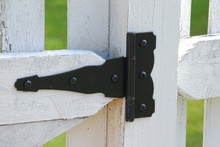Gate Hinge On A White Picket Fence. Close Up Of Black Iron Hinge.