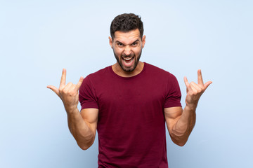 Handsome man over isolated blue background making rock gesture