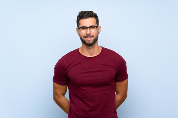 Handsome man over isolated blue background with glasses and happy