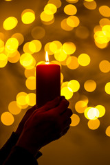 A woman is holding a red candle in her hands. In the background, lights with festive bokeh light up. Concept: festive illumination