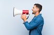 © luismolinero - Handsome man over isolated blue background shouting through a megaphone