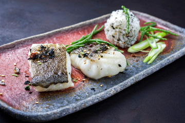 Wall Mural - Gourmet fried Japanese skrei cod fish filet with glasswort and furikake onigiri as closeup on a modern design plate