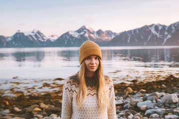 Young woman outdoors travel adventure vacations in Norway sunset mountains and fjord landscape blonde hair scandinavian girl cozy sweater and knitted hat clothing autumn season