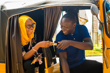 Wall Mural - young african woman sitting in the back seat of an auto rickshaw taxi paying the driver