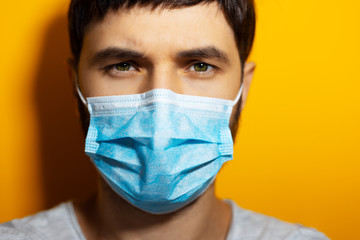 Close-up portrait of face of young man, wearing medical flu mask on orange background.