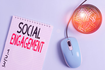 Word writing text Social Engagement. Business photo showcasing one s is degree of participation in a community or society Blank notebook and clips with computer mouse placed above pastel backdrop