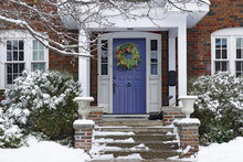  Front Door Of Snow Covered House With Christmas Wreath.