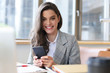 © ty - Young smiling business woman using smartphone near computer in office.
