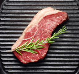 fresh raw beef steak with rosemary on black grill top view