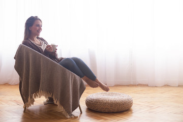 Wall Mural - Young girl enjoying coffee at home, sitting on wicker chair