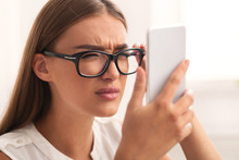 Girl Squinting Eyes Looking At Smartphone Through Eyeglasses Sitting Indoor