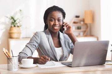 black female entrepreneur talking on mobile phone, taking notes and smiling to camera