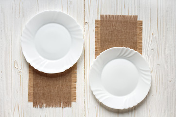 two empty plates on burlap kitchen napkins on a old white wooden table, top view