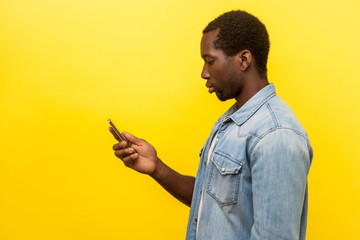 side view of serious man in denim shirt using cellphone, typing text message or dialing number with 