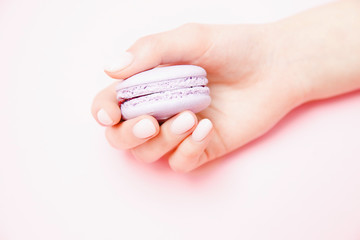 Wall Mural - Stylish trendy female manicure on pink background. Girl holds hands violet macaron cookies. Concept skin care