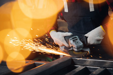 Worker hand electric saw wheel grinding on steel structure in factory, light spark