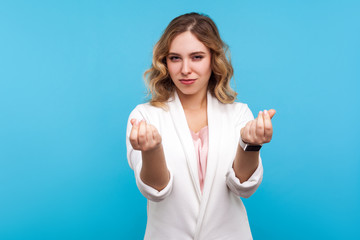 I need cash. Portrait of attractive woman with wavy hair in white jacket showing gesture of money and looking seductively at camera, asking for payment. indoor studio shot isolated on blue background