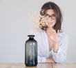 © papa - A young woman wearing glasses looks straight at the camera through a dry bouquet on the table in front of her.