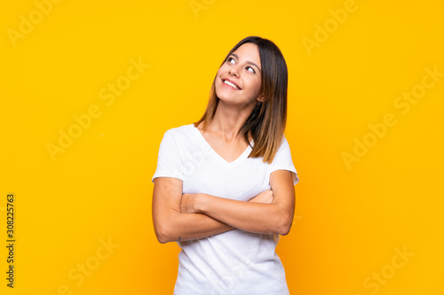Fotografía Young woman over isolated yellow background looking up while smiling