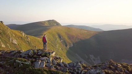 Canvas Print - Hiker standing on top of rocky mountain enjoying magnificent view. Mountaineer looking at sunrise in mountains.