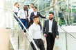 © xartproduction - young business people arego down the stairs and talking on the background of glass offices. Corporate businessteam and manager in a meeting.