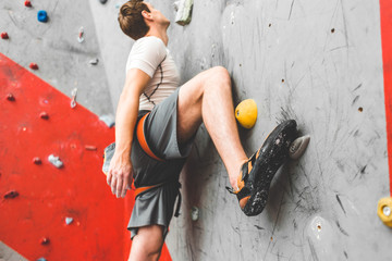 Wall Mural - Sportsman climber moving up on steep rock, climbing on artificial wall indoors. Extreme sports and bouldering concept