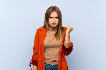 Teenager girl with coat over isolated blue background with angry gesture