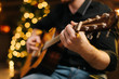 © dikushin - Male plays guitar close-up. Against the background of a decorated Christmas tree with a bokeh effect.