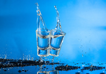 two falling glasses with vodka in motion are frozen with a spray and a splash