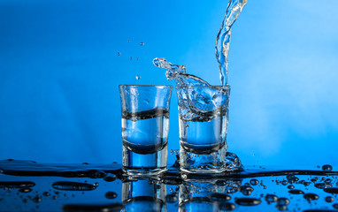 two falling glasses with vodka in motion are frozen with a spray and a splash