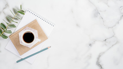 Fototapete - Home office desk with paper notepad, cup of coffee and eucalyptus leaf on marble background. Feminine workspace concept. Flat lay, top view, copy space.