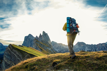 Wall Mural - young man hiking at seceda mountain peak at sunrise. backpack, yellow jacket, boots, beanie. traveli