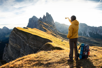 Wall Mural - young man hiking at seceda mountain peak at sunrise. backpack, yellow jacket, boots, beanie. traveli