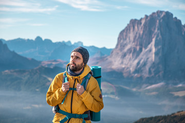 Wall Mural - young man hiking at seceda mountain peak. backpack, yellow jacket, boots, beanie. traveling to puez 