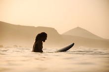 Side View Naked Man With Dreadlocks Sitting On The Surfing Board In The Sunset Time