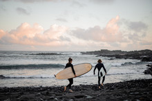 Two Man And Woman Surfers With The Surf Boards Walking On The Sea Shore