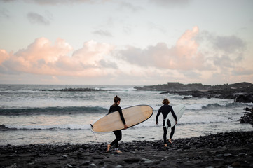 Two man and woman surfers with the surf boards walking on the sea shore