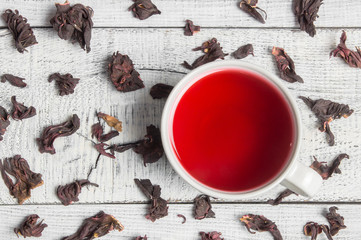 Wall Mural - White cup of healthy hibiscus tea with dried hibiscus flowers on white wooden background, winter hot drink concept for cold and flu 