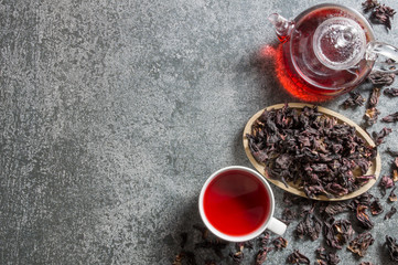 Wall Mural - White cup of healthy hibiscus tea with dried hibiscus flowers and teapot on grey rustic background, winter hot drink concept for cold and flu 